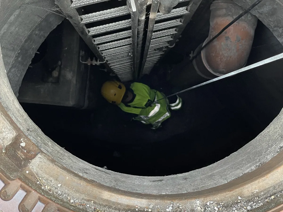 Beschäftigter mit Helm und Sicherungsseil steigt in einen Schacht ein
