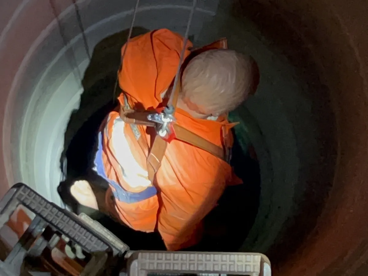 Übungspuppe im Rettungsgurt wird am Seil aus einem runden Schacht gerettet